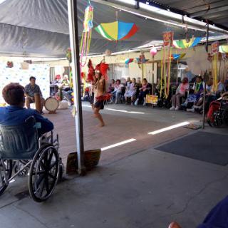A lively community performance taking place under a colorful canopy, with an audience engaged and enjoying the show.