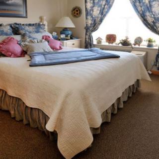 A cozy bedroom with a neatly made bed adorned with pillows and a large window with floral curtains.