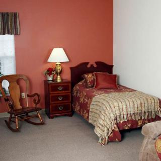A cozy bedroom featuring a single bed with patterned bedding, a rocking chair, and a nightstand with a lamp.
