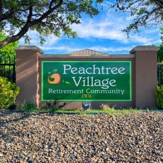 Entrance sign for Peachtree Village Retirement Community surrounded by trees and landscaping.