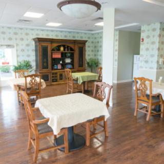 A bright dining room with wooden tables and chairs, featuring a decorated bookshelf and natural lighting.
