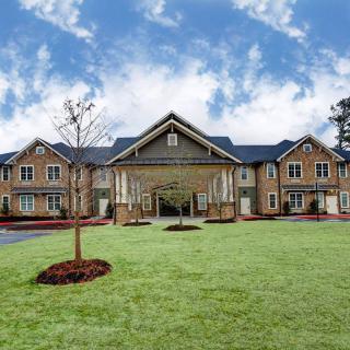 A large residential building with a neatly manicured lawn in front under a partly cloudy sky.