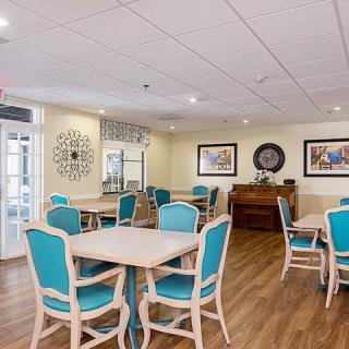 A bright and welcoming dining area featuring tables and chairs, decorated with wall art and a wooden floor.
