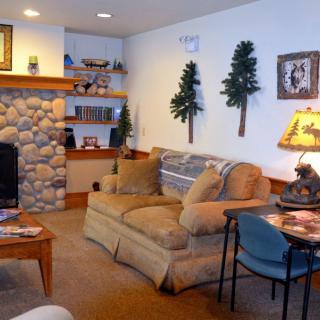 A cozy living room with rustic decor, featuring a stone fireplace, comfortable couch, and woodland-themed accents.