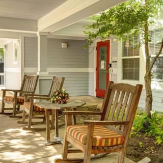 A cozy porch with wooden chairs and a red door, surrounded by greenery.