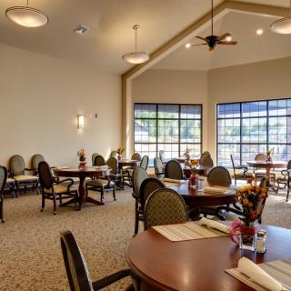 A spacious dining area with neatly arranged tables and chairs, illuminated by ceiling lights and natural daylight through large windows.
