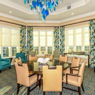 A modern dining room with stylish furniture, a chandelier, and large windows adorned with decorative curtains.