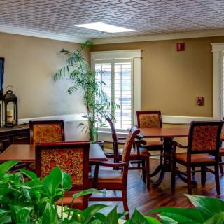 A cozy dining area with wooden tables and chairs, featuring large windows allowing natural light to illuminate the space.