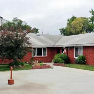 A suburban brick house with a driveway and surrounding greenery.