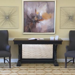 A stylish interior setup featuring two chairs flanking a console table with abstract art on the wall.