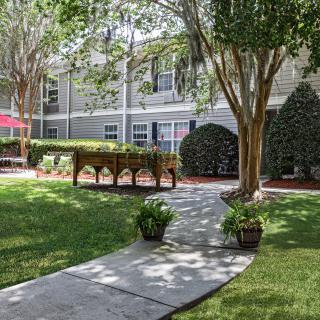 A serene garden with a winding pathway surrounded by lush greenery and residential buildings.
