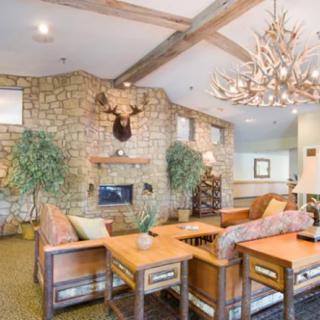 A cozy living room featuring rustic decor with a stone wall, fireplace, and wood furniture.