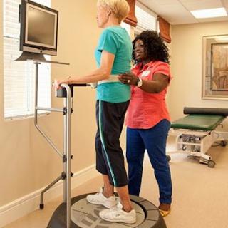 A physical therapist assists a patient on a balance training machine in a rehabilitation setting.