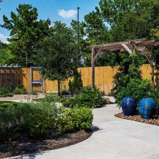A beautifully landscaped garden with a pathway, wooden fence, and vibrant potted plants.