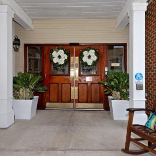 A welcoming entrance with double wooden doors adorned with wreaths, flanked by large planters and a rocking chair.