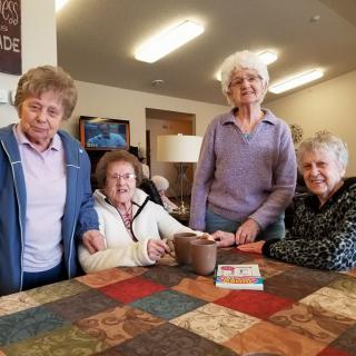 A group of elderly women gathered around a table indoors, enjoying each other's company.
