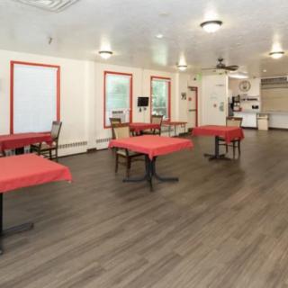 A spacious dining area with tables covered in red tablecloths and wood flooring.