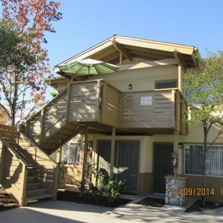An apartment building with an exterior staircase and balcony surrounded by trees.