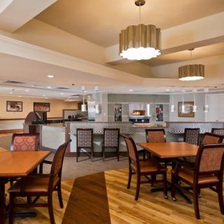 A cozy dining area with wooden flooring, tables, and chairs, illuminated by stylish lighting fixtures.