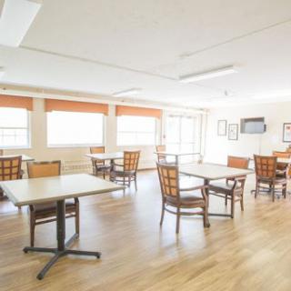 A spacious and well-lit dining area featuring simple wooden tables and chairs.