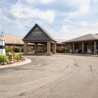 Entrance to a building with a driveway and landscaped surroundings under a cloudy sky.