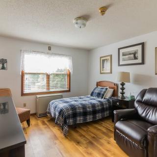 A cozy bedroom with a single bed, a leather chair, and wooden floors.