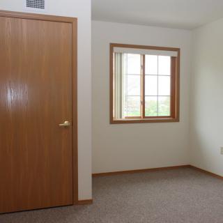 A minimalist empty room with a carpeted floor, featuring a wooden door and window.