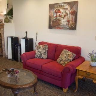 A cozy living room featuring a red sofa with floral cushions, a wooden coffee table, and a decorative painting on the wall.