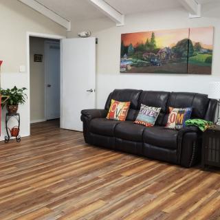 A cozy living room with a black couch, decorative pillows, wooden flooring, and scenic wall art.