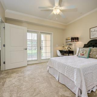 A cozy bedroom featuring a bed, desk, and ceiling fan with natural light streaming in through large glass doors.