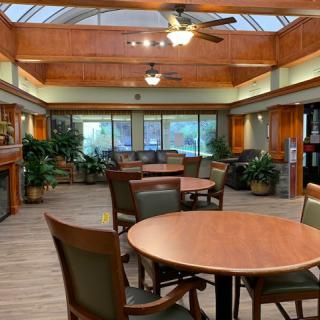 A spacious dining area with round tables, chairs, and large windows providing natural light.