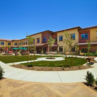 A modern building with a landscaped courtyard featuring pathways and trees under a clear blue sky.