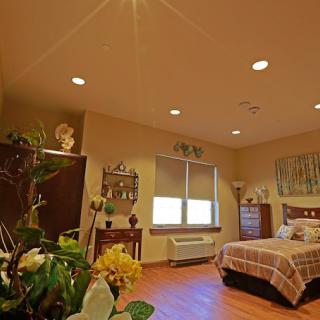 A cozy bedroom with warm lighting, featuring plants, artwork, and comfortable furniture.