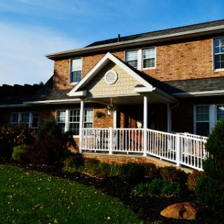 A cozy brick house featuring a welcoming front porch and well-maintained lawn.