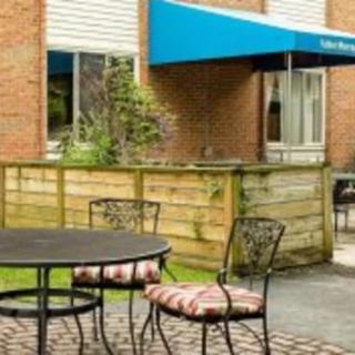 A cozy outdoor patio area with a round table and chairs in front of a brick building with a blue awning.