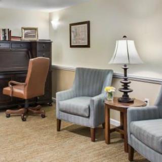 A cozy office interior with chairs, a desk, and a lamp in a well-lit room.