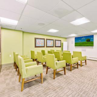 A modern waiting area featuring green chairs and a television, designed for comfort and relaxation.