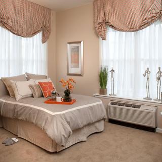 A cozy bedroom with neutral tones, featuring a well-made bed and elegant window dressings.