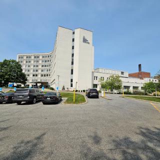 A view of a hospital building with a parking area in the foreground.