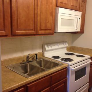 A compact kitchen setup featuring a stove, microwave, sink, and wooden cabinets.