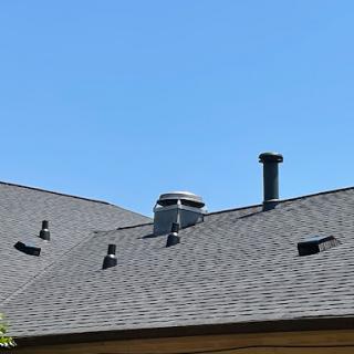 A view of a roof with various chimneys and vents against a clear blue sky.