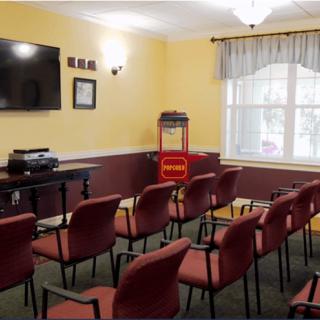 A small meeting room with rows of chairs, a television, a projector, and a popcorn machine by the window.