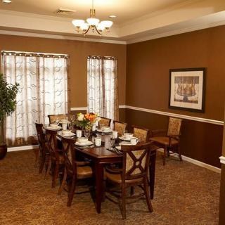 A warmly lit dining room featuring a wooden table set for eight with chairs and decorative elements.