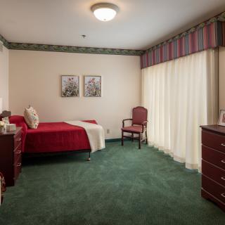 A classic-style bedroom with a single bed, green carpet, and red bedding.