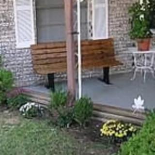 A porch with a wooden bench, flowers, and patio furniture in front of a house.