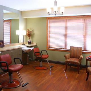 A well-lit salon with comfortable seating and large mirrors, featuring wooden flooring and elegant decor.