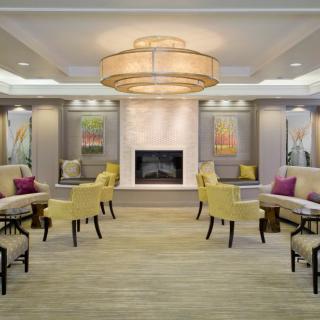 A modern lobby with a central fireplace, elegant seating, and a large chandelier.