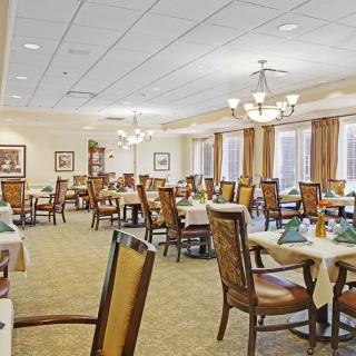A spacious dining room with elegantly arranged tables and chairs, featuring chandeliers and a carpeted floor.