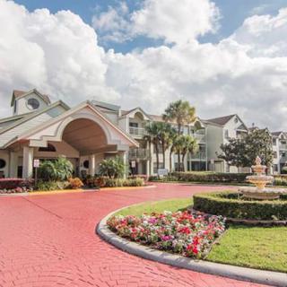 Elegant hotel entrance with a circular driveway and a central fountain under a cloudy sky.