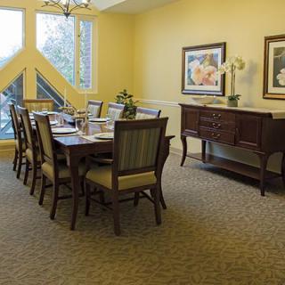 A well-lit dining room featuring a large table with chairs, decorative sideboard, and framed artwork on the walls.